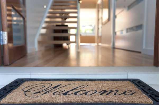 Close up of a welcome mat in front of an inviting house